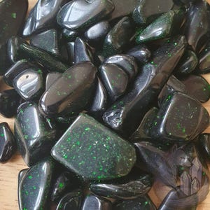 May include: A collection of glossy, black stones with green speckles. The stones are of various shapes and sizes, with smooth, rounded surfaces. The overall effect is one of natural beauty and a polished finish. These stones could be used for decoration or spiritual practices.
