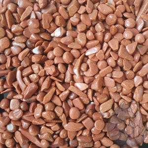 May include: A close-up of a collection of polished, reddish-brown gemstones. The stones are of various shapes and sizes, with a glittery, sparkling appearance. These gemstones are likely used for decoration or in jewellery making.