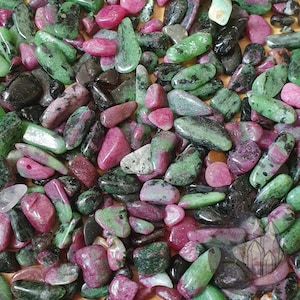 May include: A collection of tumbled gemstones in shades of green, pink, and black. The stones vary in size and shape, with a polished, smooth texture. The gemstones are scattered, creating a natural, earthy aesthetic. The image showcases a variety of ruby zoisite stones.