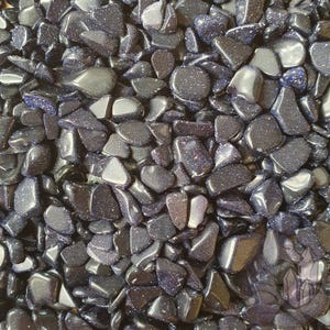 May include: A close-up of a pile of polished blue sandstone gemstones. The stones vary in size and shape, with a dark blue base colour and sparkling inclusions. The gemstones are smooth and reflective, catching the light.