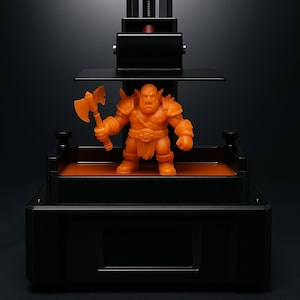 Könnte beinhalten: Orangefarbene Figur eines muskulösen Ork-Kriegers mit Axt, platziert in einem schwarzen 3D-Drucker. Der Ork hat eine detaillierte Rüstung und einen ernsten Gesichtsausdruck. Der Drucker hat einen Bildschirm und mechanische Komponenten.
