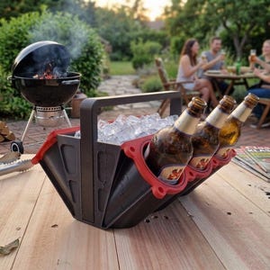 Könnte beinhalten: Ein schwarzer und roter Bierkühler gefüllt mit Eis und Bierflaschen, mit einem Griff zum einfachen Tragen. Im Hintergrund befindet sich ein Holzkohlegrill sowie eine Gruppe von Menschen, die ein Essen im Freien genießen.