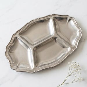 Peut inclure: Un plateau de service divisé argenté avec un bord festonné. Le plateau est divisé en trois sections et repose sur une surface en marbre blanc. Une brindille de fleurs blanches est à côté du plateau.