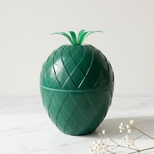 Può includere: Un secchiello per il ghiaccio verde a forma di ananas con un motivo a diamante strutturato. La parte superiore del secchiello ha un design a foglie verdi. Il secchiello per il ghiaccio è appoggiato su una superficie bianca.