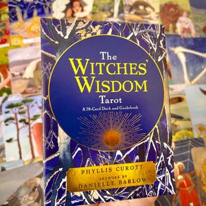 May include: The Witches' Wisdom Tarot deck box features a blue and gold design with a sunburst and the text "The Witches' Wisdom Tarot" and "A 78-Card Deck and Guidebook". The box also includes the author's name, Phyllis Curott, and the artist's name, Danielle Barlow.