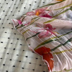 Puede incluir: Primer plano de una tela rosa transparente con estampado floral. La tela tiene un ribete blanco y est&aacute; doblada sobre s&iacute; misma. El estampado floral presenta colores rosa, naranja y verde.