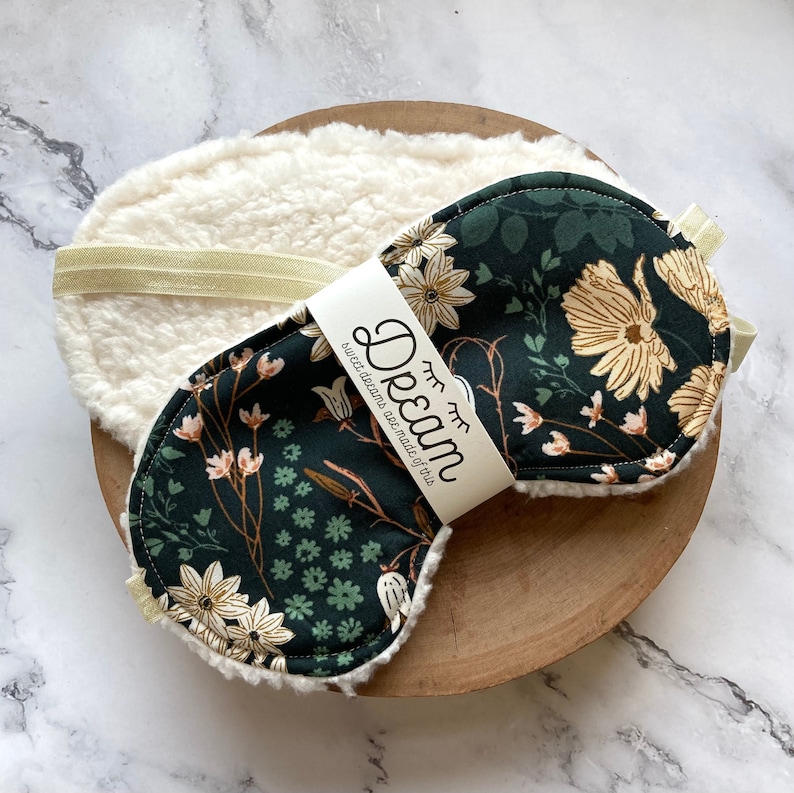 May include: A sleep mask and face pad set. The sleep mask has a dark green floral pattern with cream flowers and a soft, cream backing. The label reads "Dream". The set is designed for relaxation.
