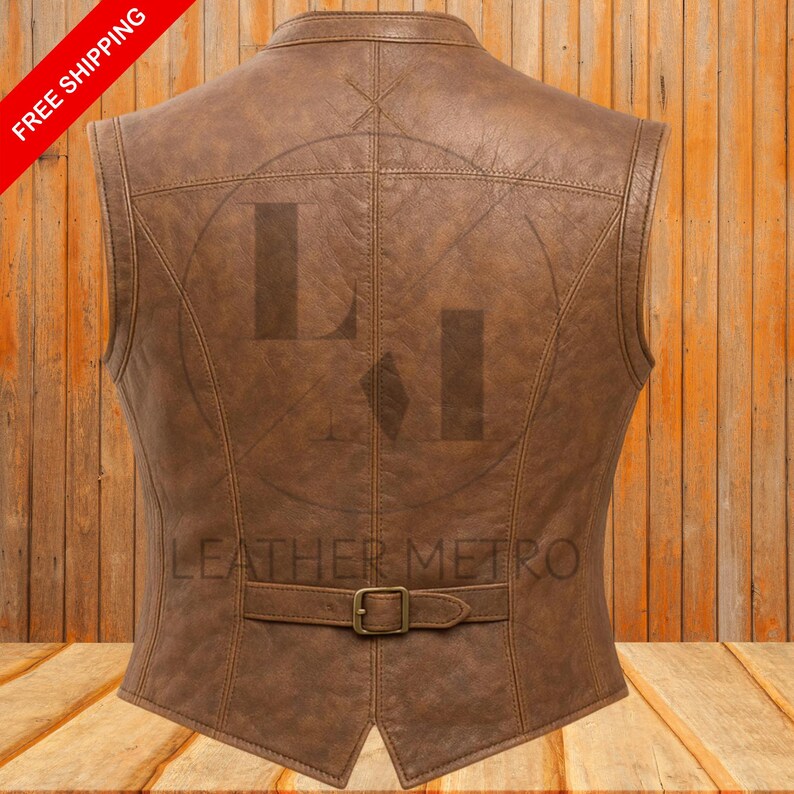 Pode incluir: Colete de couro castanho com fecho de fivela e corte sob medida. A parte de tr&aacute;s do colete apresenta um design costurado e o texto "LEATHER METRO". O colete &eacute; exibido em um fundo de madeira.