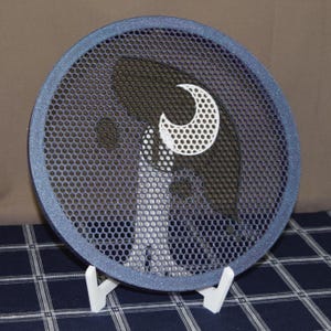 May include: A round, blue speaker cover with a mesh design and a white crescent moon shape. The speaker cover is supported by two white stands, and the background is a blue and white checkered pattern.
