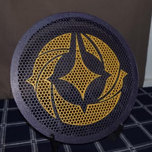 May include: A round, dark blue object with a yellow geometric design. The object has a honeycomb pattern and is supported by a black stand. The yellow design is a star-like shape with curved edges.