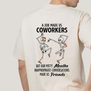 Puede incluir: Camiseta color crema con un gráfico de dos esqueletos bailando. El texto superior dice "A JOB MADE US COWORKERS" y debajo, "BUT OUR POTTY MOUTHS INAPPROPRIATE CONVERSATIONS MADE US Friends."