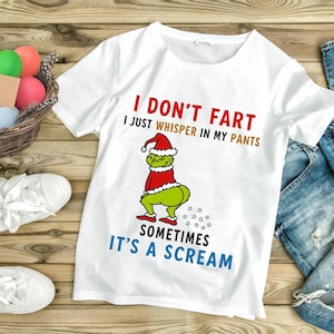 May include: White t-shirt with a humorous graphic of a green character in a Santa hat and red outfit. The text reads "I DON'T FART, I JUST WHISPER IN MY PANTS, SOMETIMES IT'S A SCREAM."