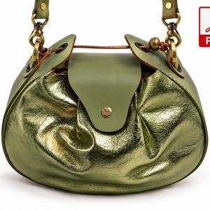 May include: A rounded handbag featuring a metallic gold finish with a soft, crinkled texture. The bag has a matte olive green leather flap closure secured with a gold-tone snap, brass hardware, and a matching olive green leather shoulder strap.