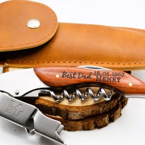 May include: A wooden and silver corkscrew with a leather case. The corkscrew has a wooden handle with the text "Best Dad 18.05.1967 HENRY" engraved on it.