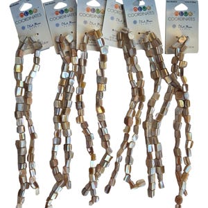 May include: Six strands of square-shaped, iridescent shell beads in shades of tan, brown, and cream. Each strand is attached to a Color Coordinates Blue Moon Beads header card with text and a circular logo at the top of each individual display.