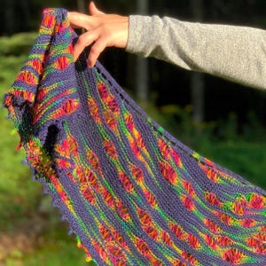 May include: A hand-knitted shawl in a deep blue hue, featuring vibrant stripes of rainbow colors. The shawl has a delicate, openwork design and a scalloped edge, showcasing a blend of textures and hues.