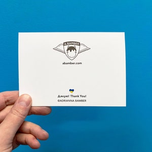 Back of Ukrainian Sunflowers Thank You Card held in hand in front of a blue wall. Illustration by illustrator Adrianna Bamber.