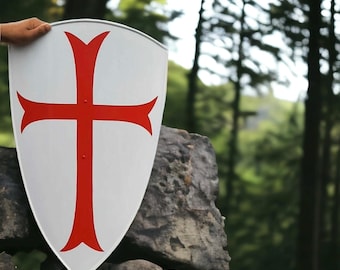 Könnte beinhalten: Ein weißes Schild mit einem roten Kreuz-Design. Das Schild wird vor dem Hintergrund von Bäumen und einer Steinmauer präsentiert. Das Schild hat eine gebogene Oberseite und eine spitze Unterseite.