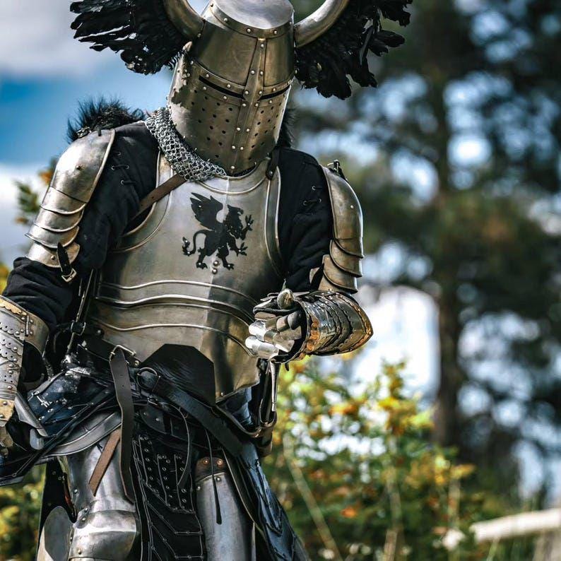 May include: A suit of medieval armor, featuring a polished metal breastplate with a black griffin emblem. The helmet has a visor and is adorned with decorative horns and black feathers. The armor includes articulated shoulder and arm pieces, and a chainmail collar.