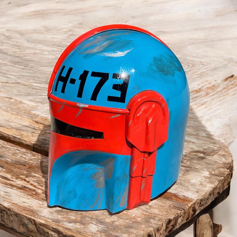 May include: A blue and red helmet with the text "H-173" in black. The helmet has a weathered appearance with visible scratches and paint wear. The design features a rounded top and angular details.