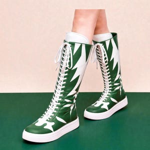 May include: Green and white knee-high boots with a leaf-like design and white laces. The boots have a white sole and are on a green surface. The boots are a unique fashion statement.