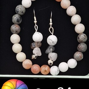May include: A jewelry set consisting of a circular beaded bracelet and two matching drop earrings. The bracelet features white, peach, and grey speckled beads. The earrings include white, grey, and clear beads. Text at the bottom reads Set 84.
