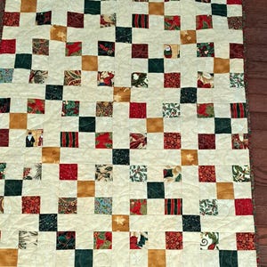 May include: A handmade Christmas quilt with a patchwork design. The quilt features squares in cream, red, green, gold, and dark brown, with various festive patterns. The quilt is machine-stitched with a quilted pattern.