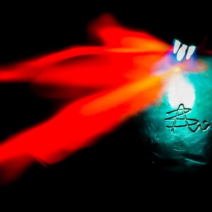 May include: A blue glass orb with a white light shining through it. The orb is surrounded by a red and orange blur.