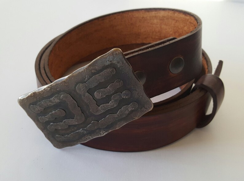 May include: A brown leather belt with a unique, textured silver buckle. The buckle features an abstract design. The belt is rolled up, showcasing the rich color and quality of the leather. A stylish accessory.