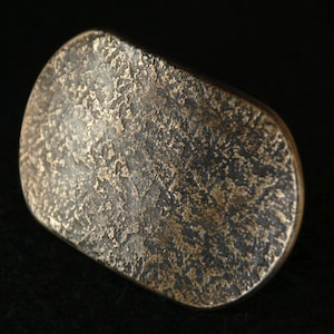 Puede incluir: Un anillo de metal de forma ovalada texturizado, de color bronce. El anillo tiene un acabado martillado rugoso.