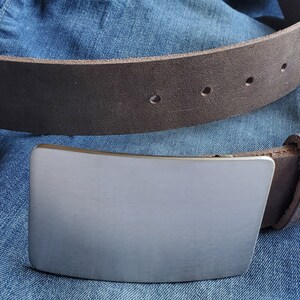 May include: A brown leather belt with a silver buckle. The buckle is rectangular and has a smooth, brushed finish.
