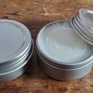 May include: Two silver metal containers with lids. One container is open and shows a white, creamy substance inside.