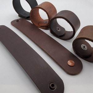 May include: Five leather bracelets in various shades of brown. Each bracelet has a metal snap closure and a small metal tag with the word "LAND" on it.