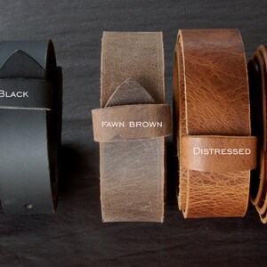 May include: Five leather belt samples in various colors: dark brown, black, fawn brown, distressed, and mahogany. Each belt has a loop with the color name printed on it. The belts are arranged horizontally against a dark background.