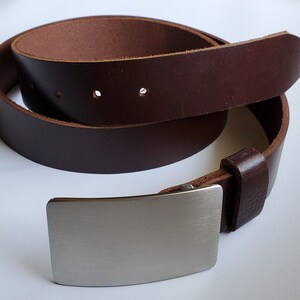 May include: A brown leather belt with a silver buckle. The belt is rolled up and the buckle is in the foreground.