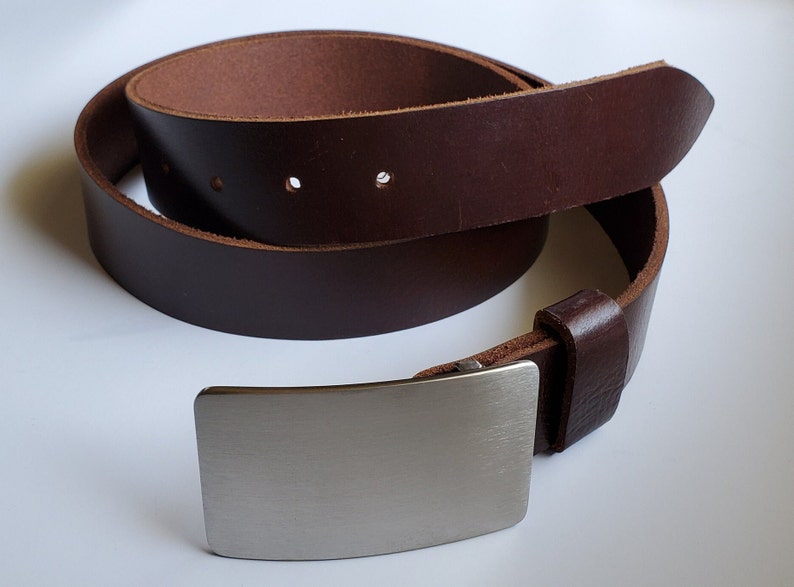 May include: A brown leather belt with a silver buckle. The belt is rolled up and the buckle is in the foreground.