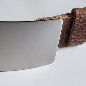May include: A brown leather belt with a silver metal buckle. The buckle is rectangular and has a smooth, brushed finish.