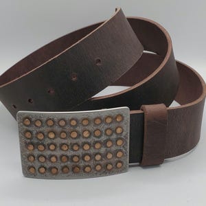 May include: A brown leather belt with a silver buckle featuring a pattern of small, round, copper-colored studs.