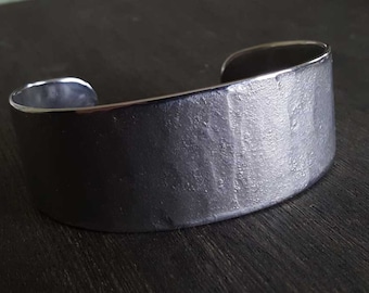 May include: A silver cuff bracelet with a textured surface.