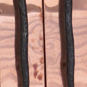 May include: Two black metal door handles with a hammered finish, mounted on a copper-coloured surface.