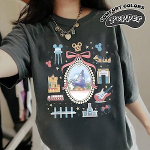 May include: Dark gray Comfort Colors t-shirt with a colorful graphic. The graphic includes a framed image of a wizard's hat, a guitar, and other themed illustrations. The text "COMFORT COLORS Pepper" is printed on the upper right.