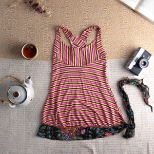 Könnte beinhalten: Ein ärmelloses Oberteil mit horizontalen Streifen in Pink, Orange und Schwarz. Das Oberteil hat einen Saum mit Blumenmuster und einen gekreuzten Rücken. Ein schwarzer und floraler Schal, eine Vintage-Kamera und eine Teekanne sind ebenfalls im Bild.
