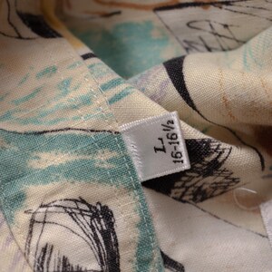 May include: Close-up of a patterned fabric with a tag. The fabric features a mix of colors, including cream, teal, and black, with abstract designs. The tag reads "L 16-16 1/2".