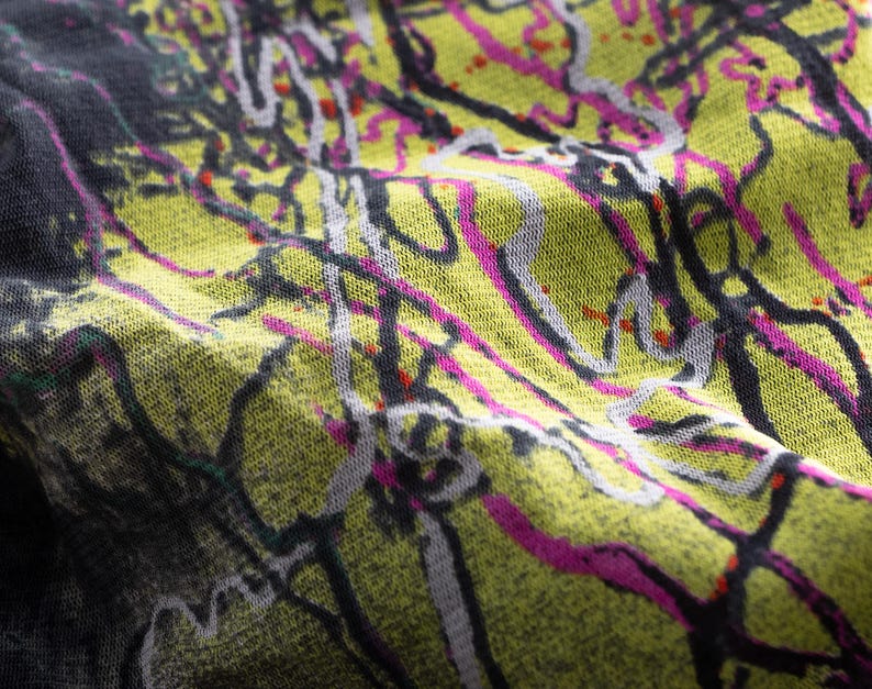 May include: Close-up of a fabric with an abstract design. The pattern has a yellow-green base with black, white, and pink lines and splatters. The fabric appears soft and textured, with visible folds and creases.