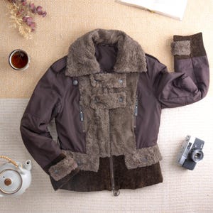 Könnte beinhalten: Braune Jacke mit Kunstfellkragen und Front. Die Jacke hat einen Reißverschluss, zwei Vordertaschen und einen dunkelbraunen unteren Einsatz. Die Ärmel haben dunkelbraune Manschetten. Eine Vintage-Kamera und eine Tasse Tee liegen neben der Jacke.