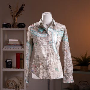 May include: A white ceramic mug with a black handle and the text "But First, Coffee" in a bold, black font. The mug is set against a blurred background, suggesting a cozy setting.