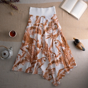 May include: White skirt featuring a brown parrot pattern. The skirt has a white waistband and an asymmetrical hem. The fabric looks lightweight. A teapot, teacup, and a wooden duck ornament are also visible.