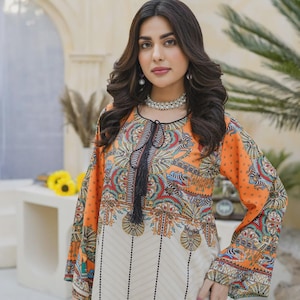 May include: An orange and cream-colored tunic with a detailed, colorful pattern. The long-sleeved top features a black tassel tie at the neckline and a vertical striped design on the lower portion. The sleeves and upper chest area have a vibrant, ornate design.