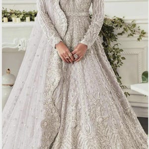 Puede incluir: Un vestido formal de color lavanda claro con intrincados bordados y abalorios plateados. El vestido de manga larga presenta un corpiño ajustado, una falda amplia y un chal a juego. Adecuado para ocasiones especiales.