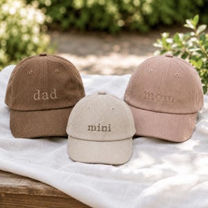 Puede incluir: Tres gorras de béisbol de pana en color marrón, beige y rosa empolvado. La gorra marrón tiene bordado el texto 'dad', la beige 'mini' y la rosa empolvado 'mom'. Cada gorra cuenta con una visera curva y ojales de ventilación cosidos.